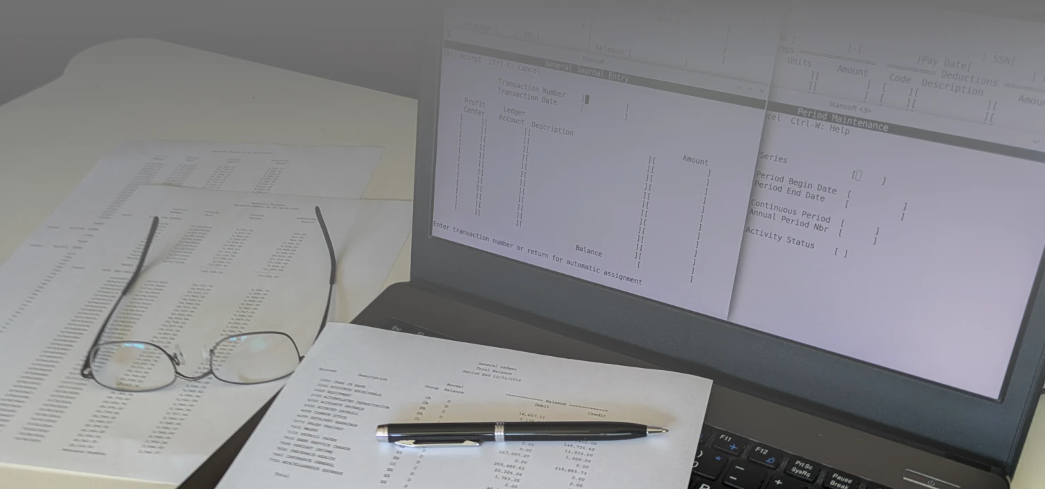 Photo of a laptop on a desk displaying terminals running Stansoft with printed reports on the desk. A pen and eye glasses are on top of the reports.